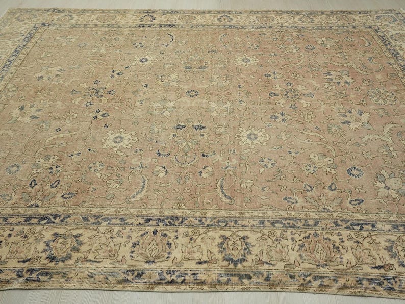 a large, intricately patterned rug with a floral design in shades of beige and blue. The rug is spread out on a wooden floor, and the border is a darker shade of blue.