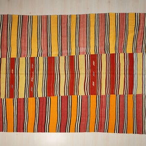 a vibrant, colorful textile with vertical stripes in various shades of red, yellow, and orange. The pattern is composed of multiple panels, creating a visually striking and intricate design.