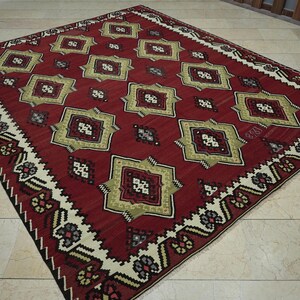 a large, intricately patterned rug with a red and gold color scheme, placed on a tiled floor.