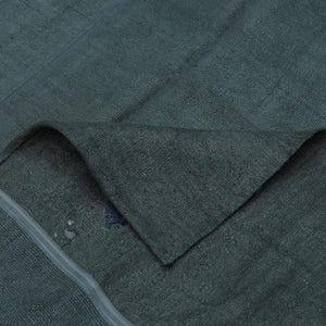 a close-up view of a dark green fabric, possibly a blanket or garment, with a small blue stain on it.
