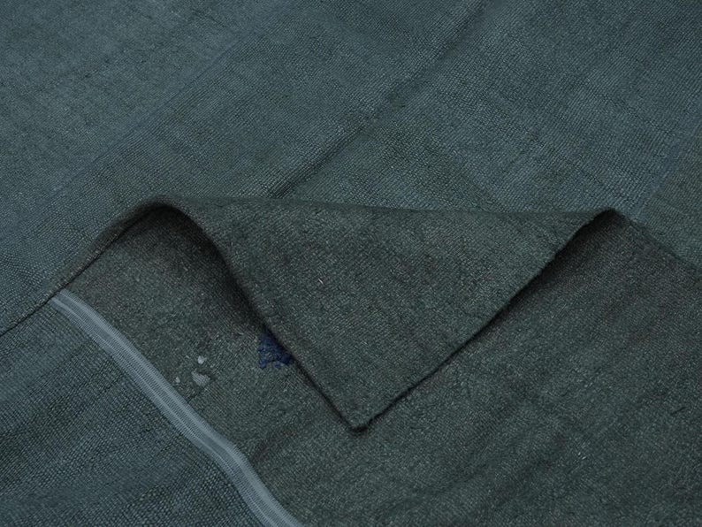a close-up view of a dark green fabric, possibly a blanket or garment, with a small blue stain on it.