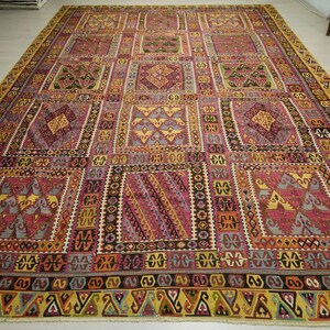 a large, intricately patterned rug with a variety of geometric shapes and designs in shades of pink, yellow, and orange. The rug is spread out on a white floor, creating a striking contrast with the colorful patterns.