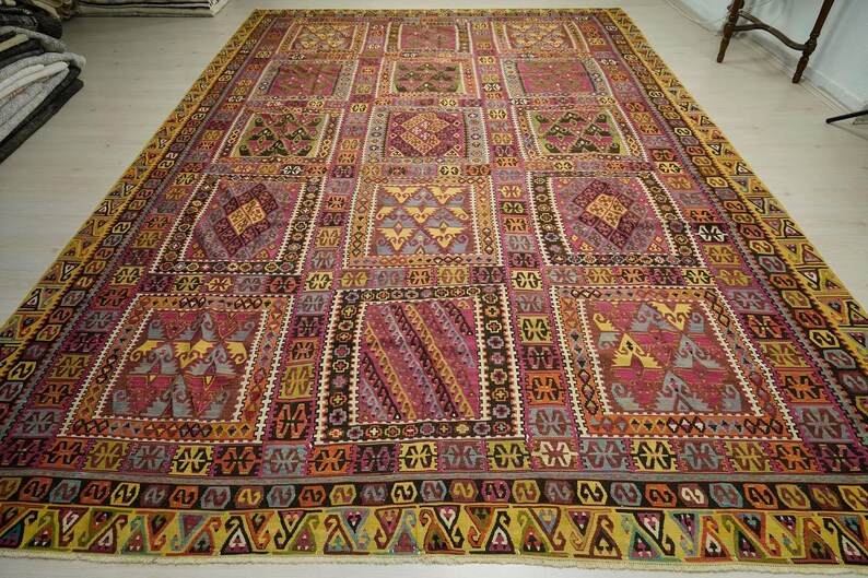 a large, intricately patterned rug with a variety of geometric shapes and designs in shades of pink, yellow, and orange. The rug is spread out on a white floor, creating a striking contrast with the colorful patterns.