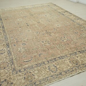 a large, intricately patterned rug with a beige and blue color scheme, placed on a wooden floor.