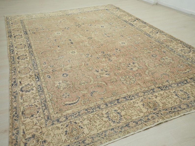 a large, intricately patterned rug with a beige and blue color scheme, placed on a wooden floor.