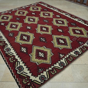a large, intricately patterned rug with a red and gold color scheme, placed on a tiled floor.