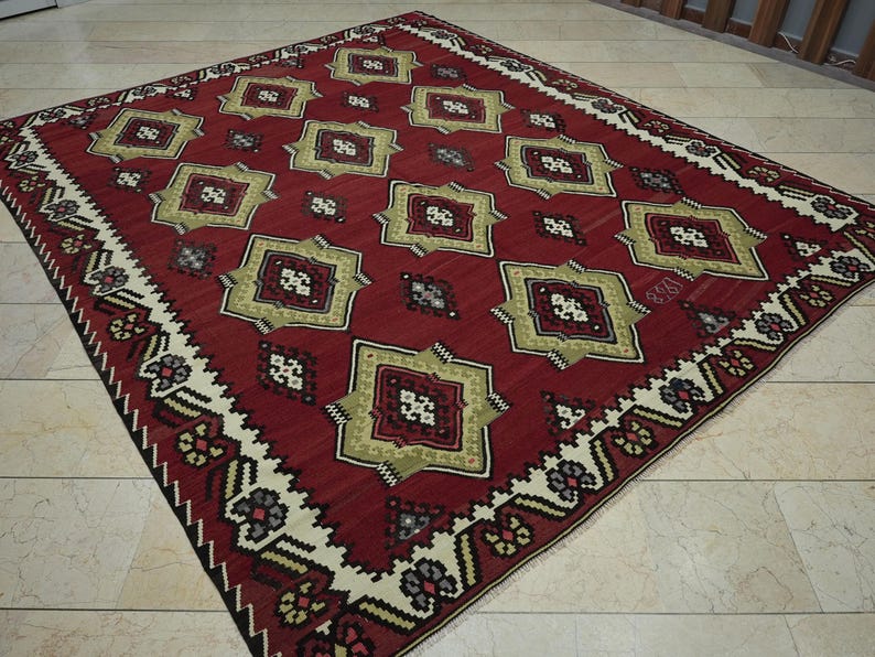 a large, intricately patterned rug with a red and gold color scheme, placed on a tiled floor.