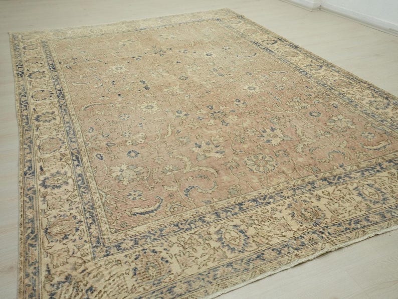a large, intricately patterned rug with a beige and blue color scheme, placed on a wooden floor.