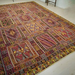 a large, intricately patterned rug with a variety of geometric shapes and designs in shades of pink, yellow, and red. The rug is spread out on a white floor, creating a striking contrast with the colorful patterns.