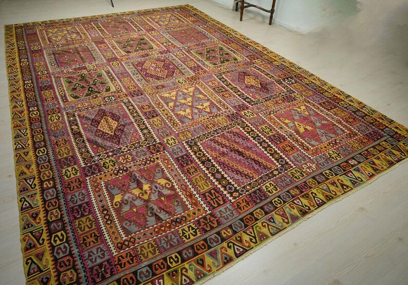 a large, intricately patterned rug with a variety of geometric shapes and designs in shades of pink, yellow, and red. The rug is spread out on a white floor, creating a striking contrast with the colorful patterns.