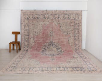 May include: A large rectangular area rug featuring a faded dusty rose centre with a central dark blue floral medallion. The rug has a wide beige border with intricate dark blue floral patterns and a secondary outer border in dusty rose.