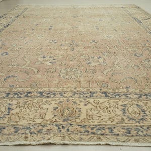 a large, intricately patterned rug with a floral design in shades of pink and beige. The rug is placed on a wooden floor, and the perspective of the image is from above, providing a detailed view of the rug's design and texture.