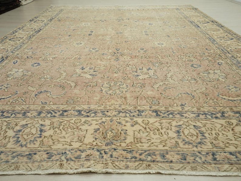 a large, intricately patterned rug with a floral design in shades of pink and beige. The rug is placed on a wooden floor, and the perspective of the image is from above, providing a detailed view of the rug's design and texture.