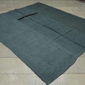 a large, square-shaped, dark green textile, possibly a blanket or rug, lying on a tiled floor.