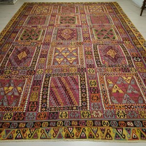 a large, intricately patterned rug with a variety of geometric shapes and designs in shades of pink, yellow, and red. The rug is spread out on a white floor, creating a striking contrast with the colorful patterns.