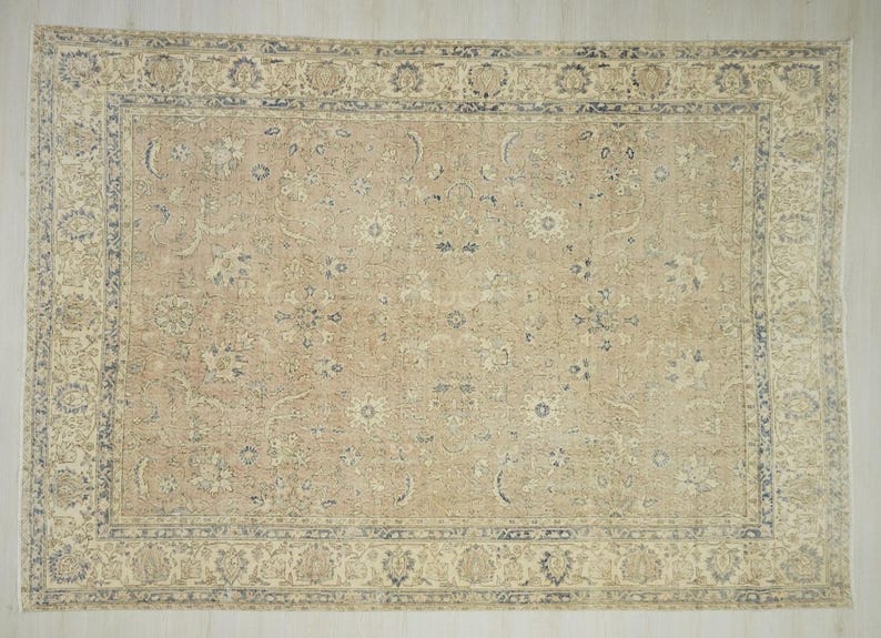 a large, intricately patterned rug with a beige and blue color scheme. The rug has a detailed design with floral and geometric patterns, and it is placed on a white surface.