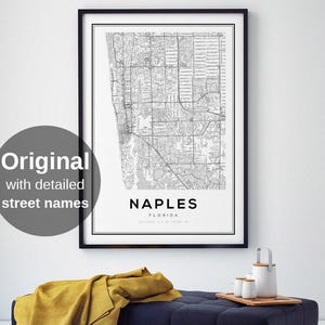 May include: A framed black and white map print of Naples, Florida, with detailed street names. The print hangs above a navy blue tufted bench with a yellow blanket and a wooden tray with white ceramic items.