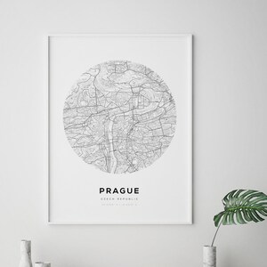 May include: A black and white map of Prague, Czech Republic, in a circular design. The map is printed on white paper and framed in a white frame. The text "PRAGUE" and "CZECH REPUBLIC" is printed below the map.