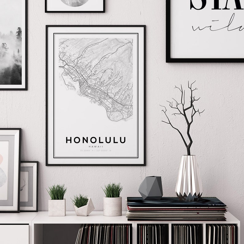 K&ouml;nnte beinhalten: Ein Schwarzwei&szlig;-Kartenabdruck von Honolulu, Hawaii, mit dem Stadtnamen und den Koordinaten unter der Karte. Der Druck ist in einem schwarzen Rahmen gerahmt und h&auml;ngt an einer wei&szlig;en Wand. Unter dem Druck befinden sich Pflanzen und eine Vase mit Zweigen auf einem wei&szlig;en Regal.