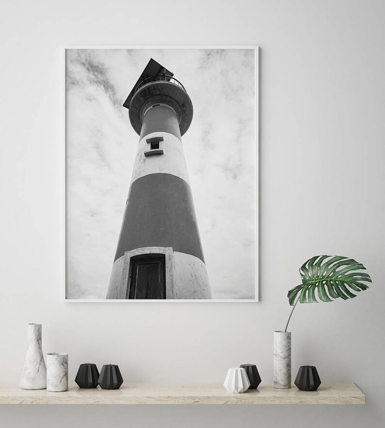 May include: Black and white photograph of a lighthouse against a cloudy sky. The lighthouse is tall and has a white and gray striped exterior. The photo is taken from a low angle, looking up at the lighthouse.