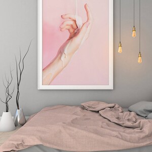 Pu&ograve; includere: Una stampa artistica incorniciata raffigurante una mano con una sostanza bianca che vi si versa sopra, su uno sfondo rosa. L'opera d'arte &egrave; esposta sopra un letto con un copriletto rosa e lenzuola grigie. Sono visibili lampadine a sospensione.