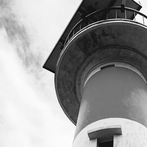 May include: A black and white photo of a tall, round, concrete tower with a metal railing at the top. The tower is against a cloudy sky.