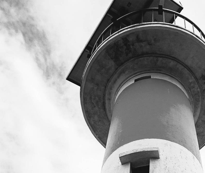 May include: A black and white photo of a tall, round, concrete tower with a metal railing at the top. The tower is against a cloudy sky.