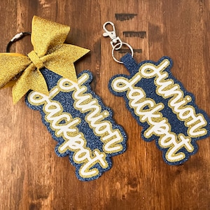 May include: Two blue and gold glitter keychains with the text "Junior Jackpot" in white. One keychain has a gold glitter bow attached.