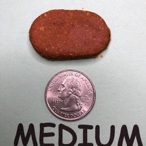 May include: A medium-sized, oval-shaped, orange-brown dog treat. The treat is about the size of a US quarter.