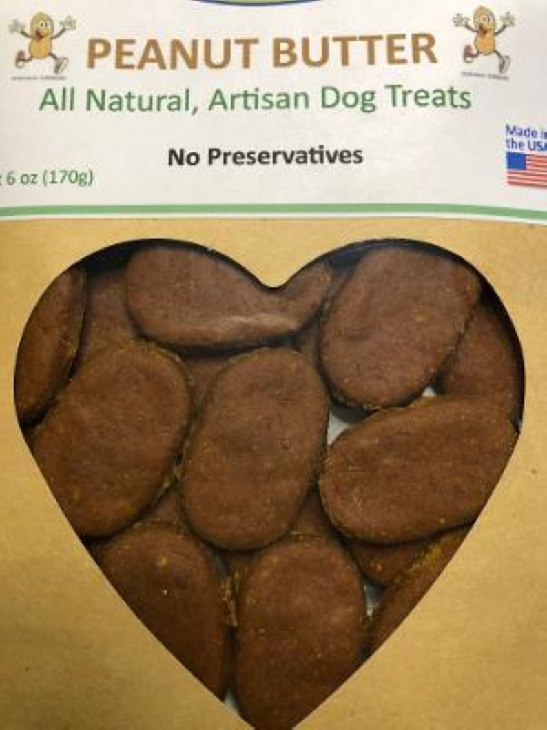 May include: A heart-shaped package of peanut butter dog treats. The treats are brown and oval-shaped. The package is labeled "Peanut Butter All Natural, Artisan Dog Treats No Preservatives 6 oz (170g) Made in the USA."