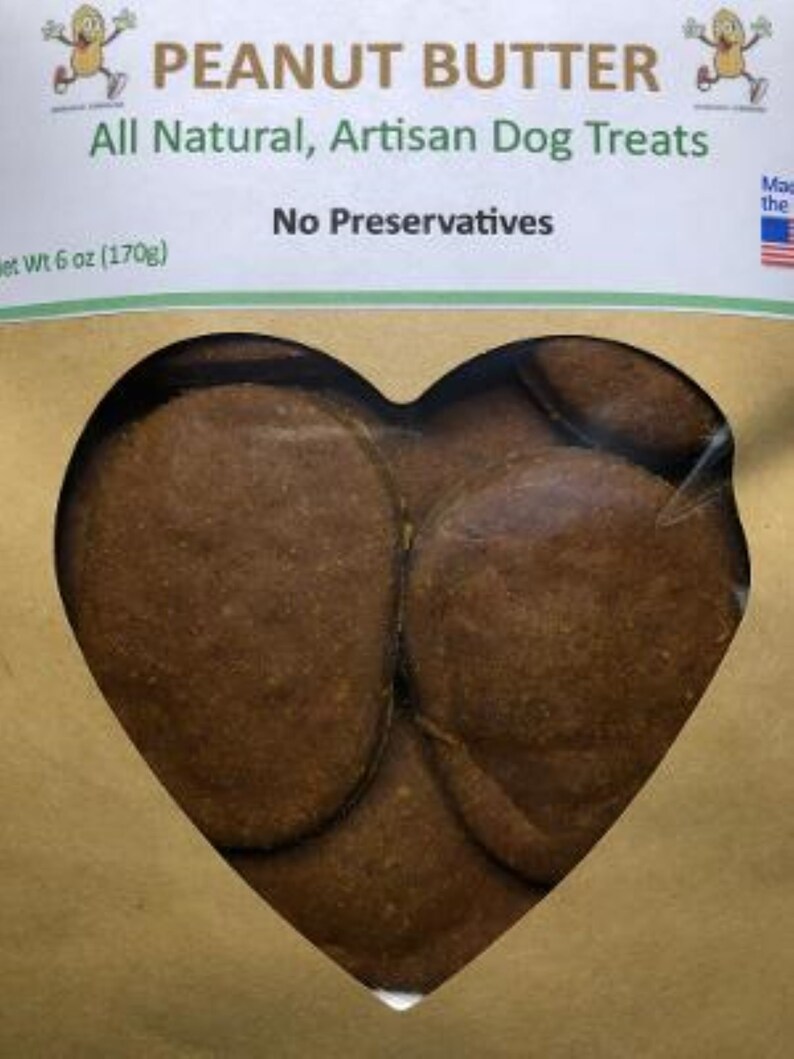 May include: A brown paper bag with a heart-shaped window showing peanut butter dog treats. The bag has the text "PEANUT BUTTER" in large letters and "All Natural, Artisan Dog Treats" in smaller letters. The bag also has the text "No Preservatives" and "Net Wt 6 oz (170g)".