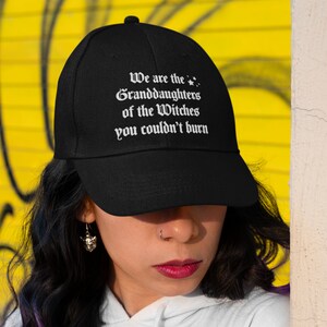 May include: A black baseball cap with white embroidered text that reads "We are the Granddaughters of the Witches you couldn't burn".