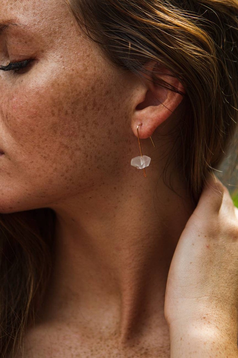 May include: A pair of gold earrings with a clear, faceted crystal pendant. The earrings are simple and elegant, perfect for everyday wear.