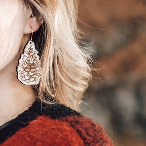 Puede incluir: Un par de pendientes de tono dorado con un diseño de piña de madera.