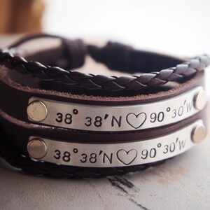 May include: A brown leather bracelet with two silver bands engraved with the coordinates "38° 38'N ♥ 90° 30'W".