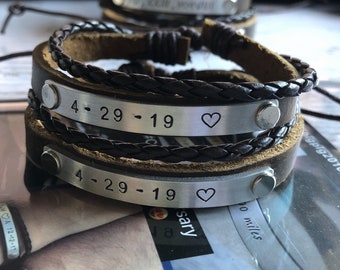May include: Two brown leather bracelets with silver metal bands. The bands are engraved with the date "4-29-19" and a heart symbol.