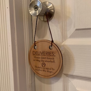 May include: A wooden sign with the text "DELIVERIES: Please don't knock or ring the doorbell. There's no need to involve the dogs..." and a paw print graphic.