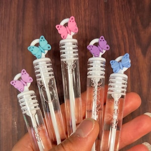 May include: Five clear plastic bubble wands with butterfly-shaped tops in pink, purple, and blue. The wands have white plastic rings around the middle and white plastic wands inside.