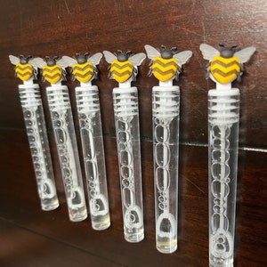 May include: Six clear plastic bubble wands with yellow and black bee-shaped tops. The wands are filled with bubble solution.