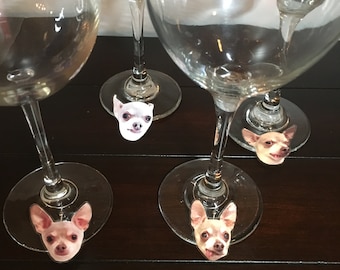 May include: Four clear wine glasses with small dog face stickers on the bottom of each glass. The stickers are of different colored dogs.