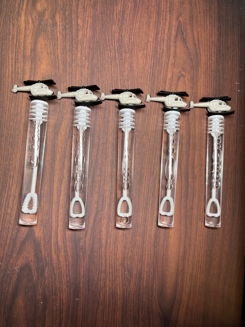 May include: Five clear plastic bubble wands arranged in a row. Each wand features a white plastic helicopter topper with black rotor blades. The wands have a long, transparent cylindrical tube containing a white bubble wand applicator inside.