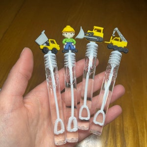 May include: Four clear plastic bubble wands with different construction vehicle and worker figurines on top. The wands have white bubble wands attached to the bottom.