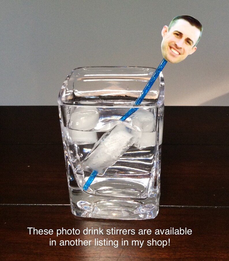 Puede incluir: Un agitador de bebidas de pl&aacute;stico azul con una foto de una persona en la parte superior. El agitador est&aacute; en un vaso de agua con cubitos de hielo.