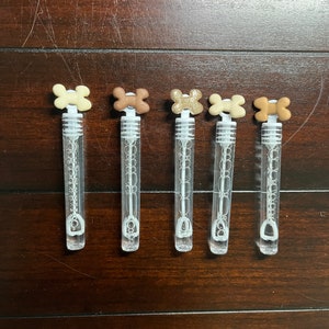 May include: Five clear plastic bubble wands with different colored bone-shaped tops. The tops are brown, beige, gold, white, and brown.