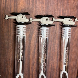 May include: Three clear plastic bubble wands, each topped with a light gray helicopter featuring black rotors and the word RESCUE embossed on the side. The wands contain clear bubble solution and a white internal wand with a circular loop at the base.