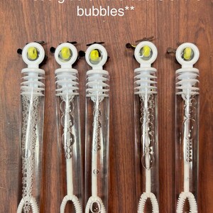 May include: Five clear plastic bubble wands with white caps and internal white wands. Each cap features a small yellow and black helicopter topper. Text reads: Back View: Small yellow and black helicopters, please note you will see glue on the backs of the bubbles**