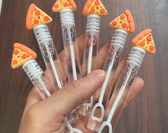 May include: Five clear plastic bubble wands, each topped with a small, three-dimensional pizza slice charm. The charms feature orange crusts, yellow cheese, and red pepperoni details. Each wand contains a white plastic bubble blower stick.
