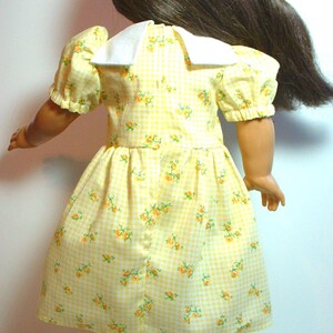 May include: A yellow gingham dress with a white collar and small floral print. The dress has puffed sleeves and a gathered skirt.