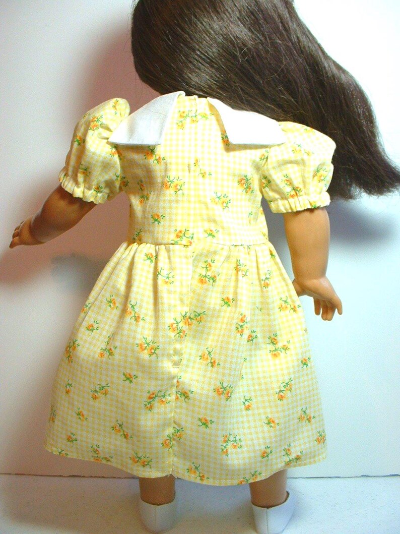 May include: A yellow gingham dress with a white collar and small floral print. The dress has puffed sleeves and a gathered skirt.