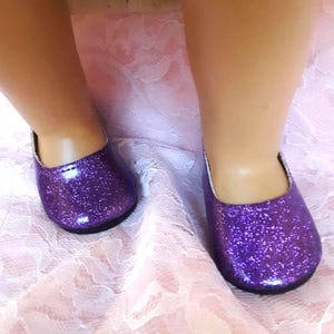 May include: A pair of purple glitter shoes with a shiny finish. The shoes are flat and have a rounded toe.